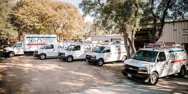 White service vans parked outside of a building, under trees. Company logos are visible.