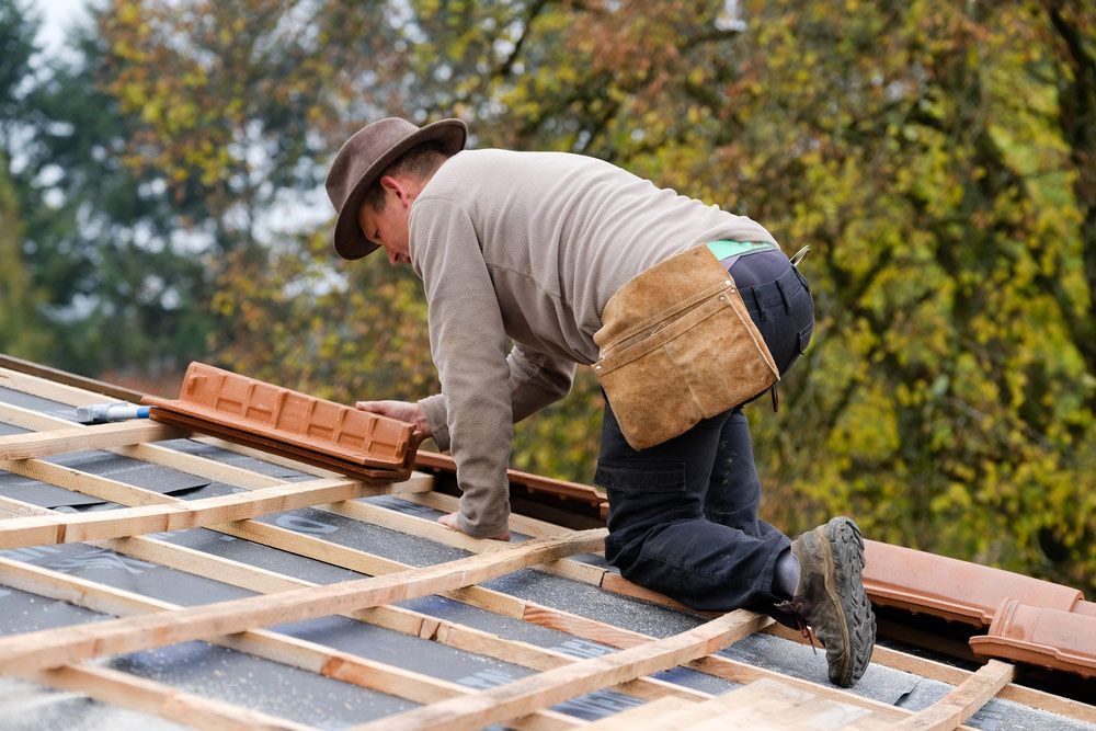A Man is Kneeling on a Roof While Installing Tiles — SRV Roofing In Kingaroy, QLD