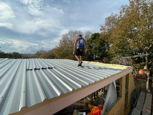 Man With A Blue Top Walking On The Roof — Expert Roofers in Maroochy River, QLD
