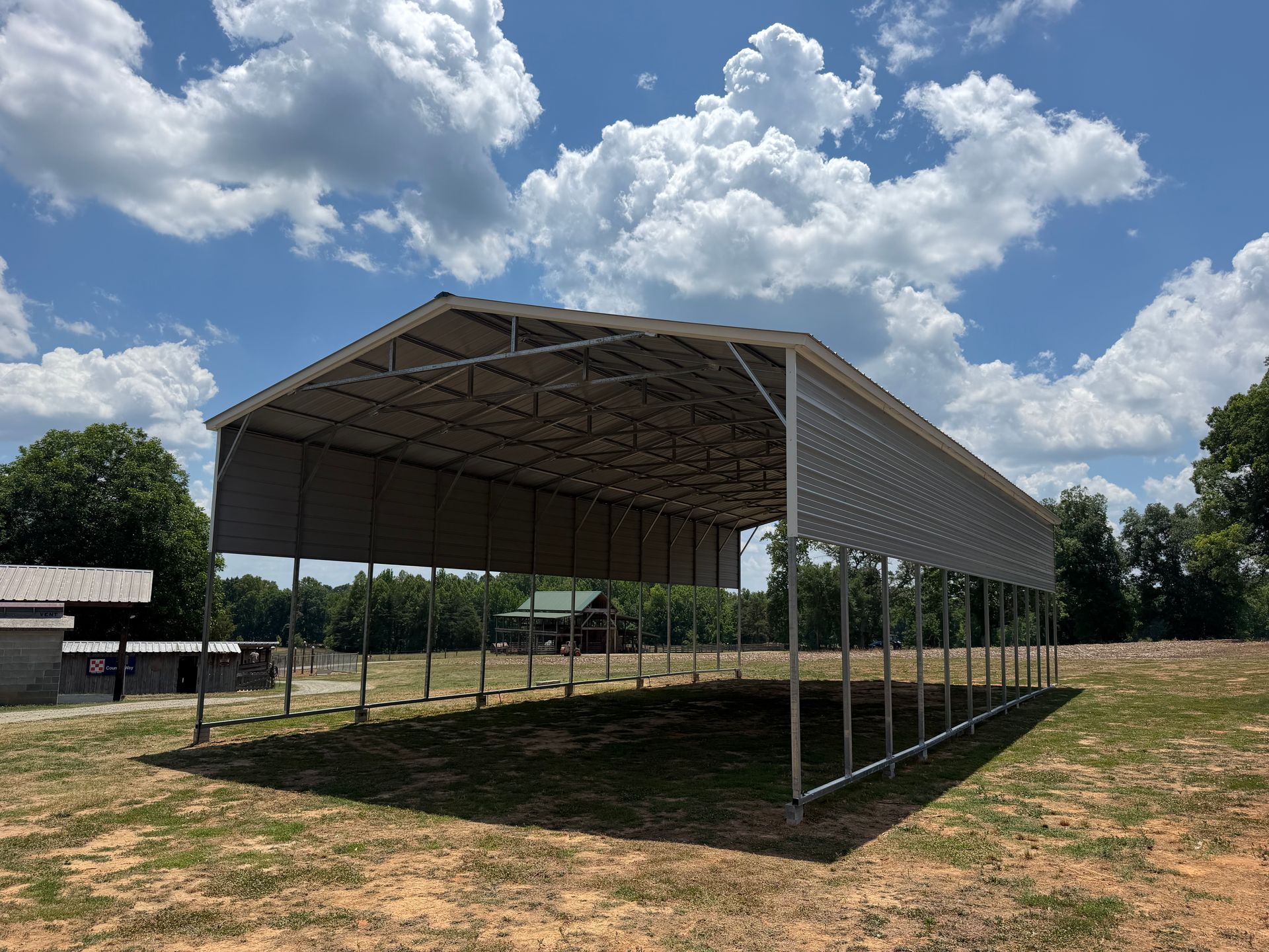 Open-sided metal pavilion on a grassy field under a blue, cloudy sky