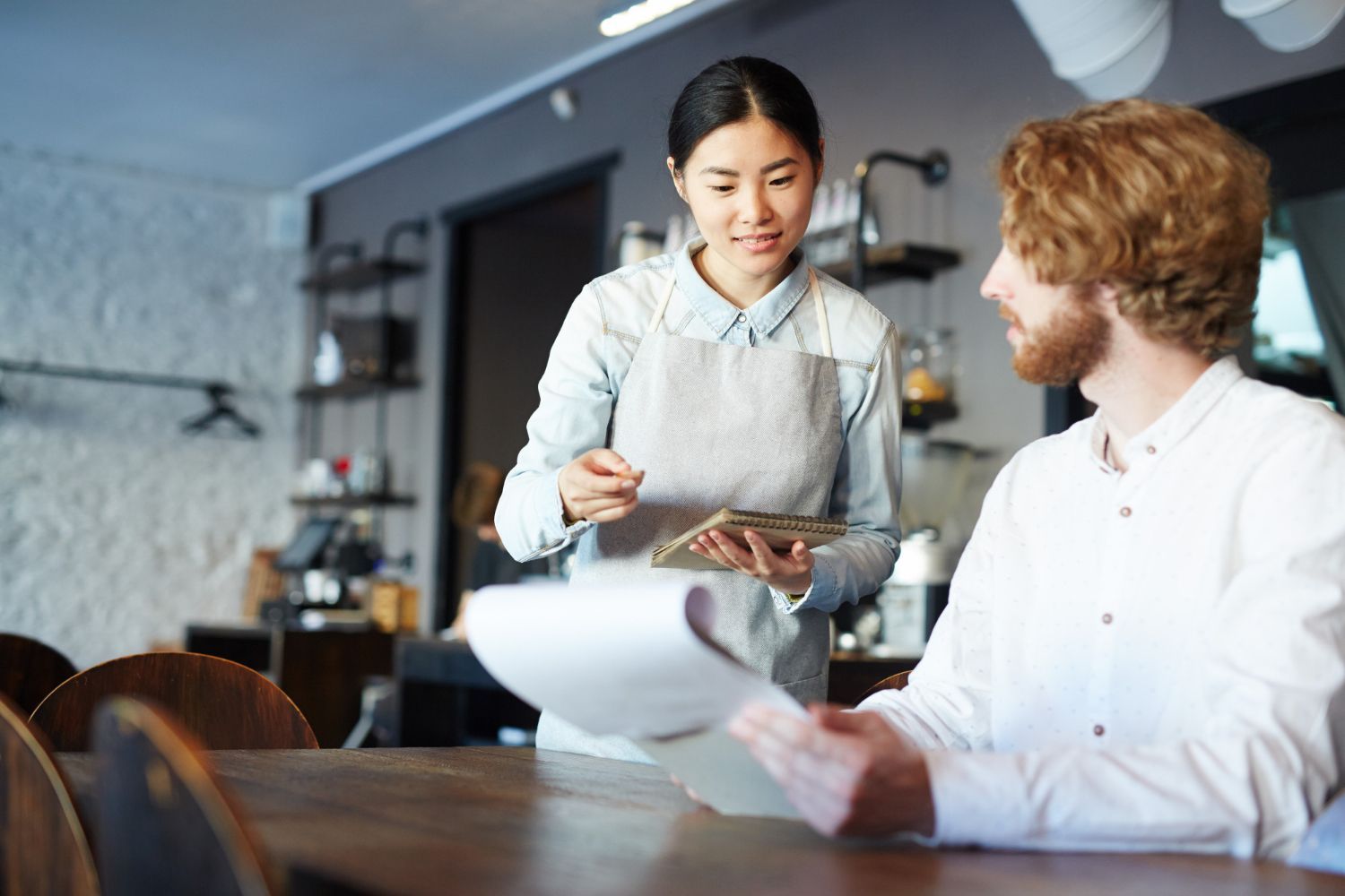 Waitress taking an order at a restaurant table. She holds a tablet and pen while looking at the customer.