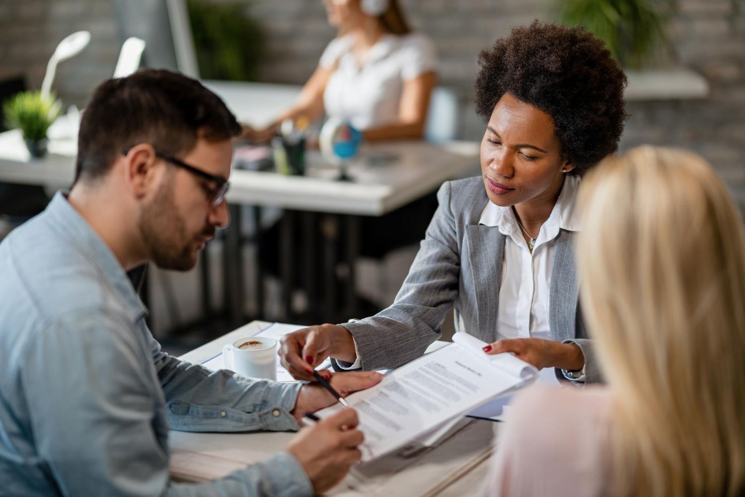 Businesswoman showing paperwork to a couple at a desk in an office setting.