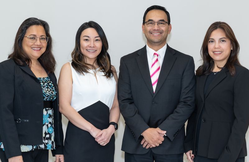 Four people in business attire standing in front of a white wall, smiling.