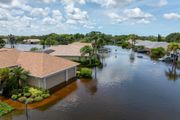 Flooded suburban neighborhood with brown water covering streets and yards, under cloudy sky.