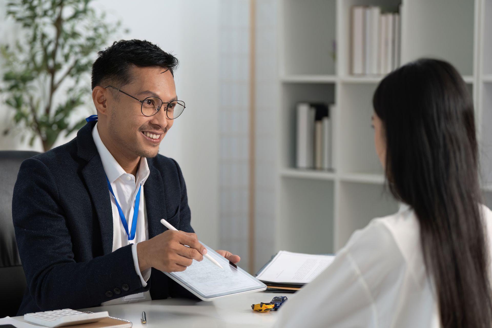 Man in glasses shows tablet to woman at desk. Office setting.