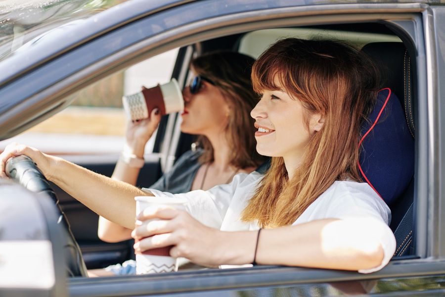 Two people in a car; driver holding a drink, passenger drinking.
