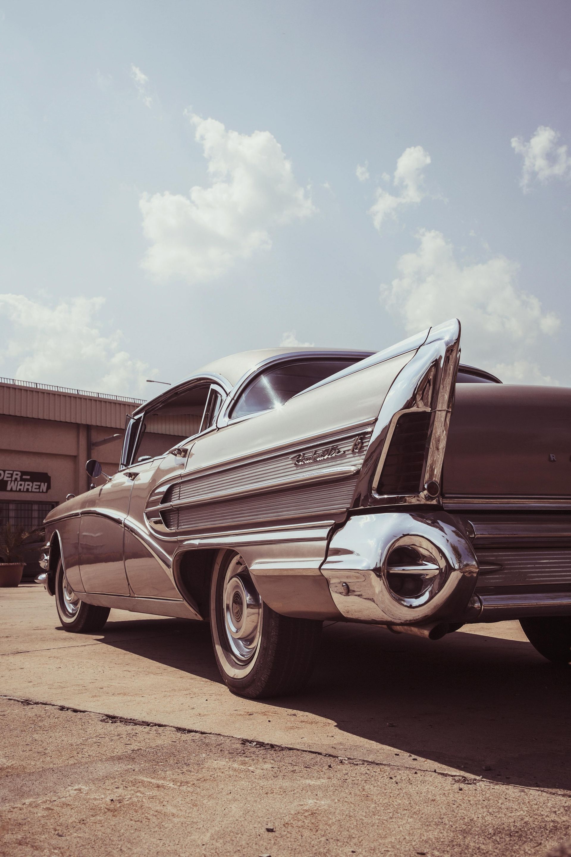 Vintage silver and brown car with large tail fins, parked outside on a sunny day.