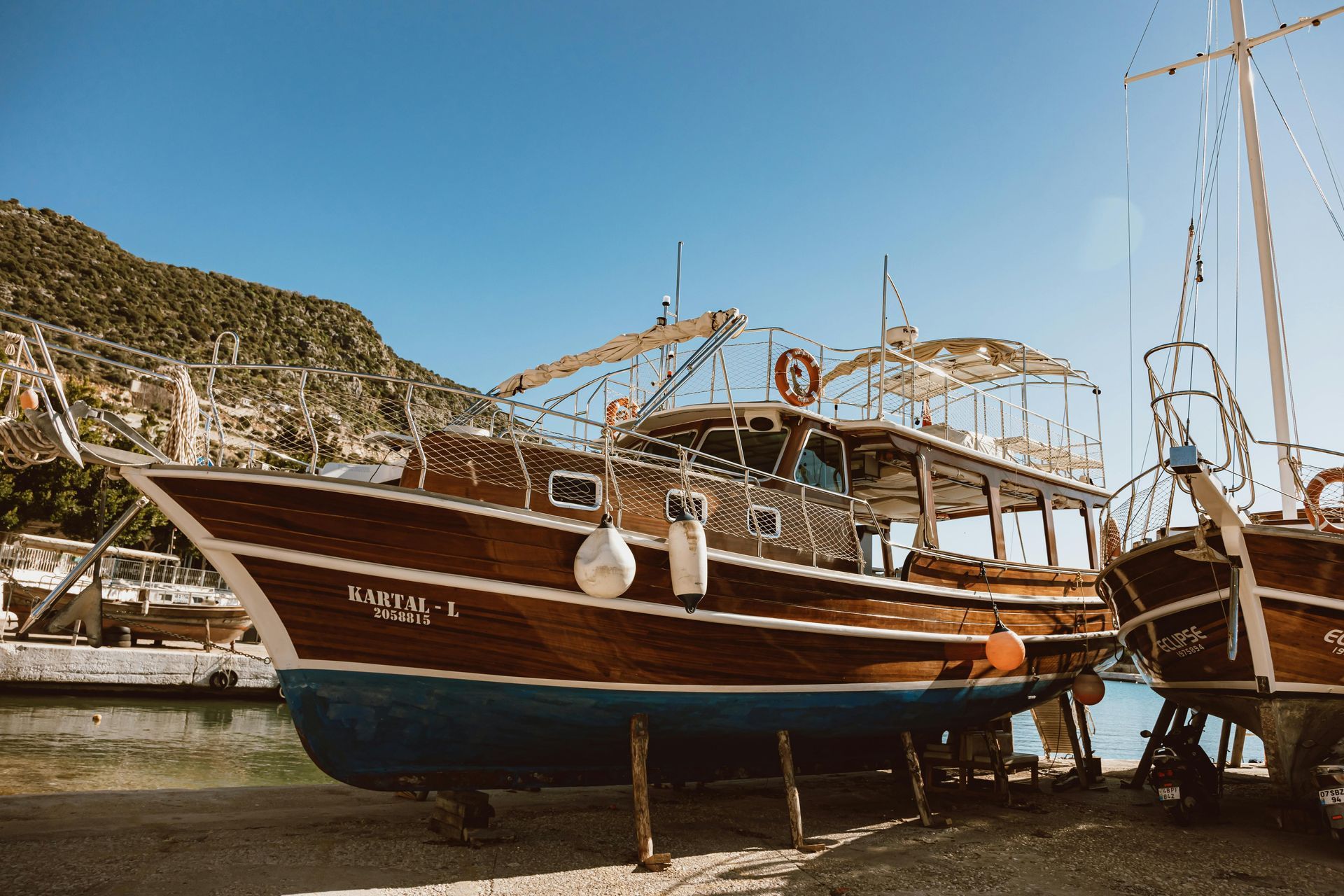 Wooden boats docked on dry land with blue hulls. Clear blue sky and hillside in the background.