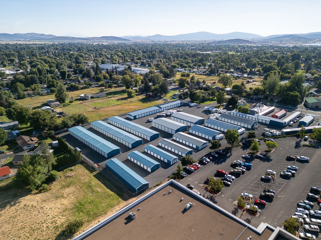Aerial view of storage units with blue doors, surrounded by parking and a suburban landscape.