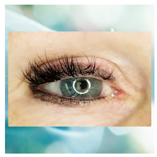 Close-up of an eye with long, dark eyelashes. The eye is light blue with a ring light reflection.