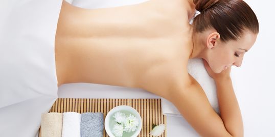 Woman receiving a massage, lying face down on a massage table. Towels and bowl of flowers on a bamboo tray.
