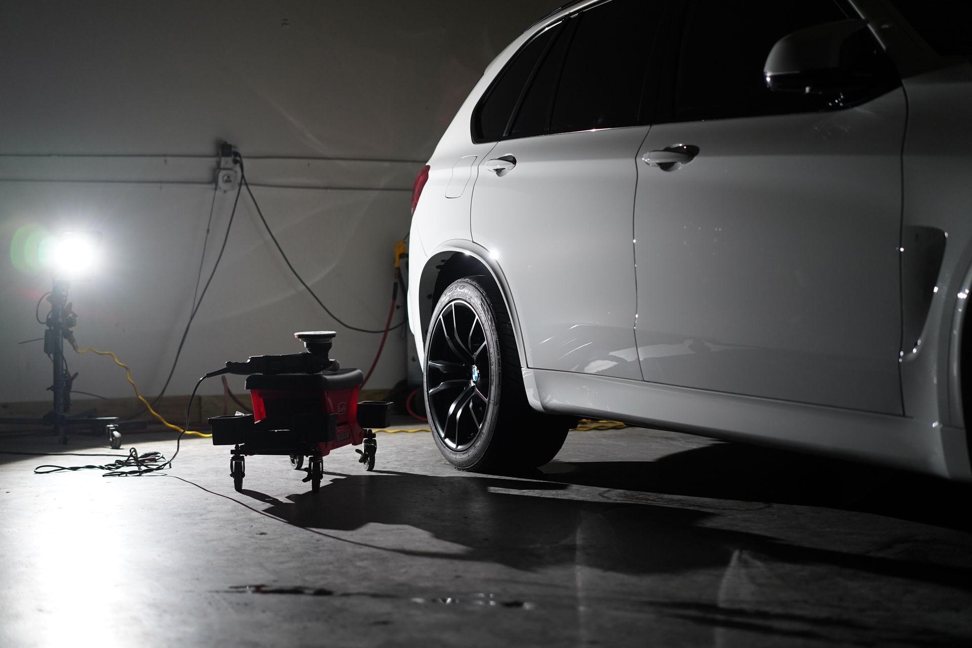 White SUV in a garage being worked on, with equipment in front of it. The vehicle has black rims.