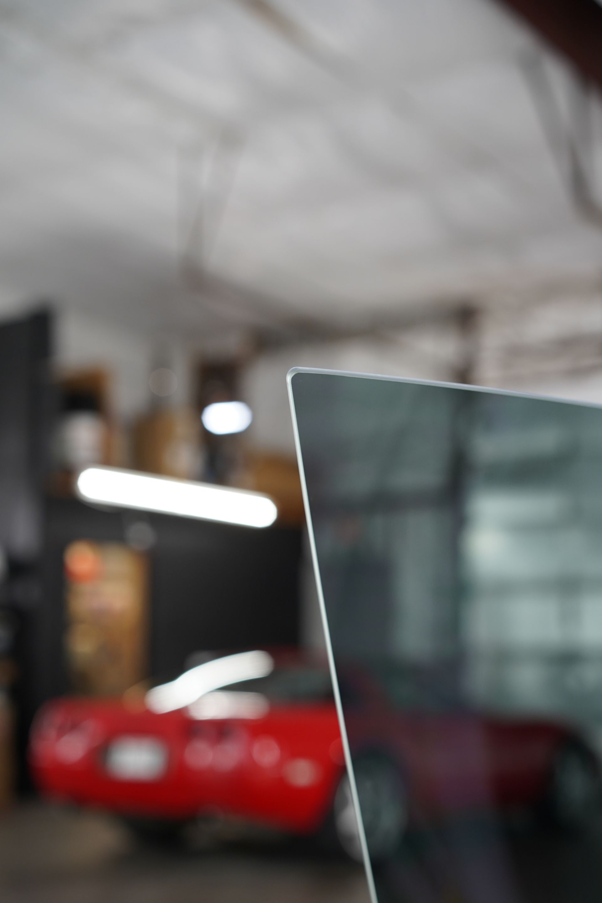 Close-up of a dark-tinted window corner, with a blurred red car and workshop interior visible in the background.