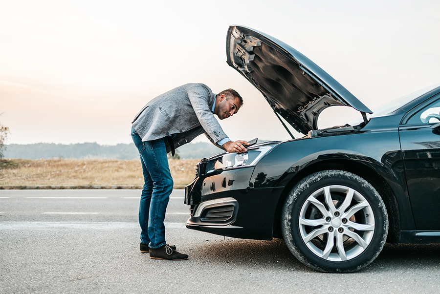 Man leaning over open hood of black car on roadside, inspecting engine
