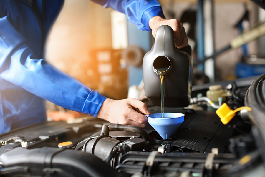 Mechanic pouring engine oil into a car through a blue funnel in a garage