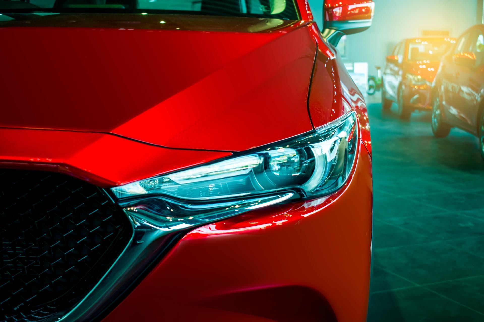 Close-up of a red car front headlight with a blurred vehicle in the background
