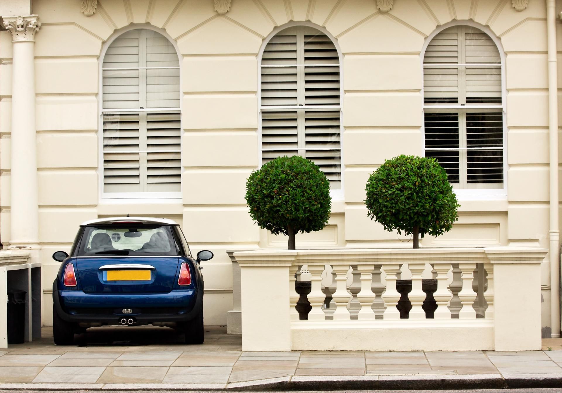 Blue car parked beside white townhouse with arched windows and two trimmed trees