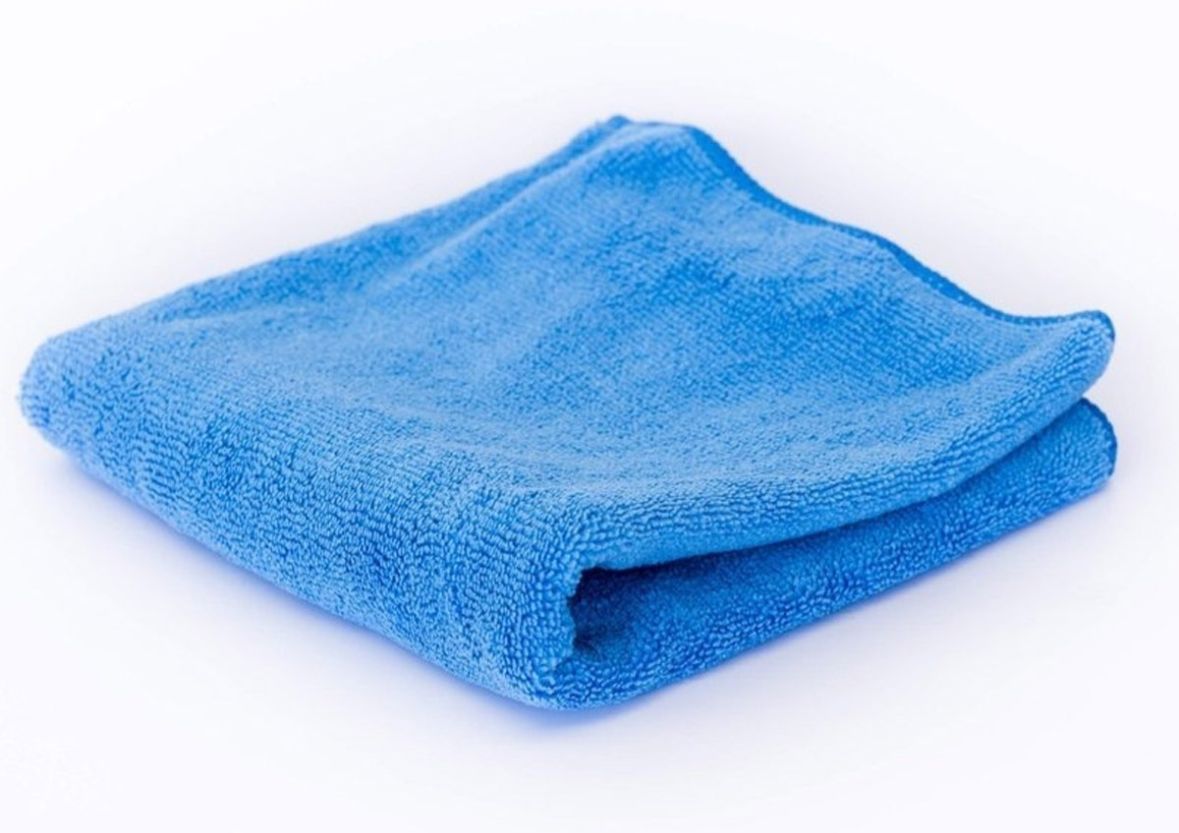 Paño de limpieza de microfibra azul, doblado cuidadosamente sobre una superficie blanca.