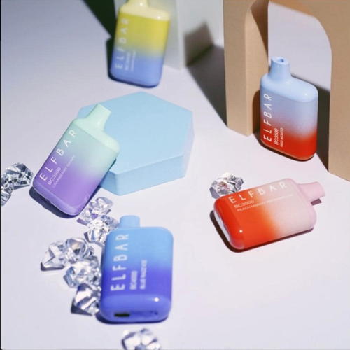 Various Elf Bar disposable vapes on a dark blue surface, different colors, with warning label.
