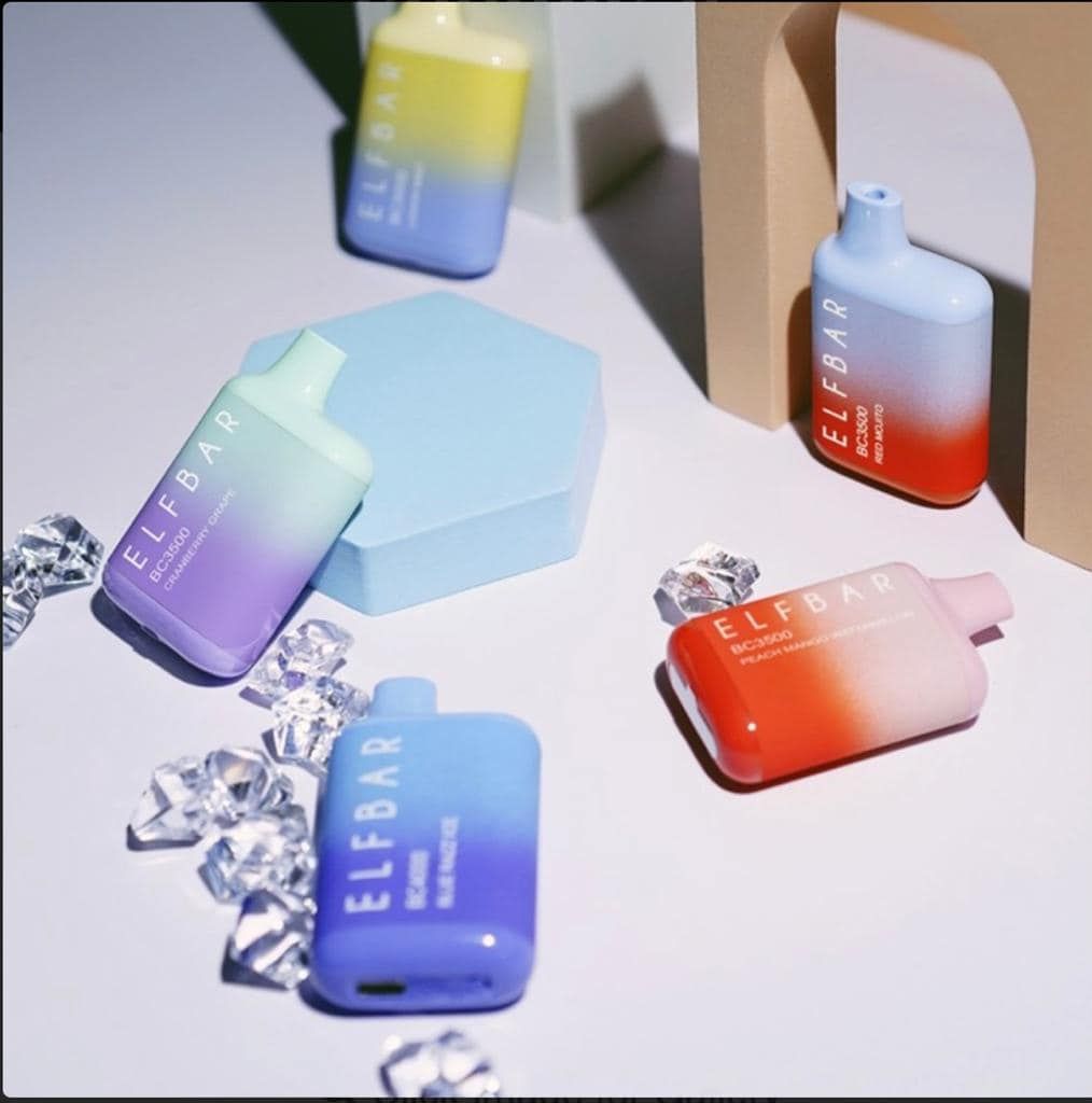 Various colorful Elf Bar disposable vapes arranged on a surface with ice crystals and a blue block.