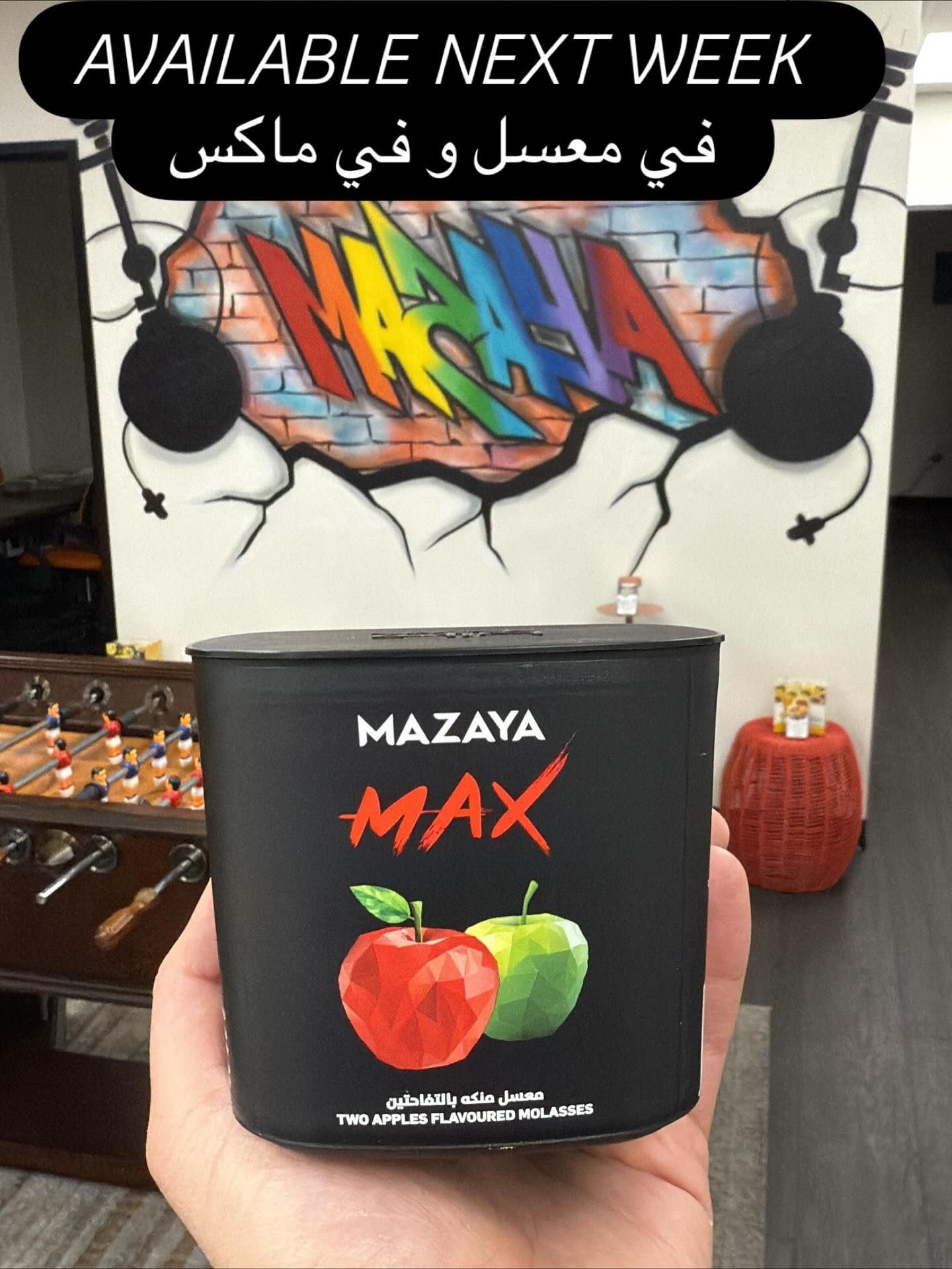 Black container of Mazaya Max apple flavored tobacco held in hand, graffiti background.