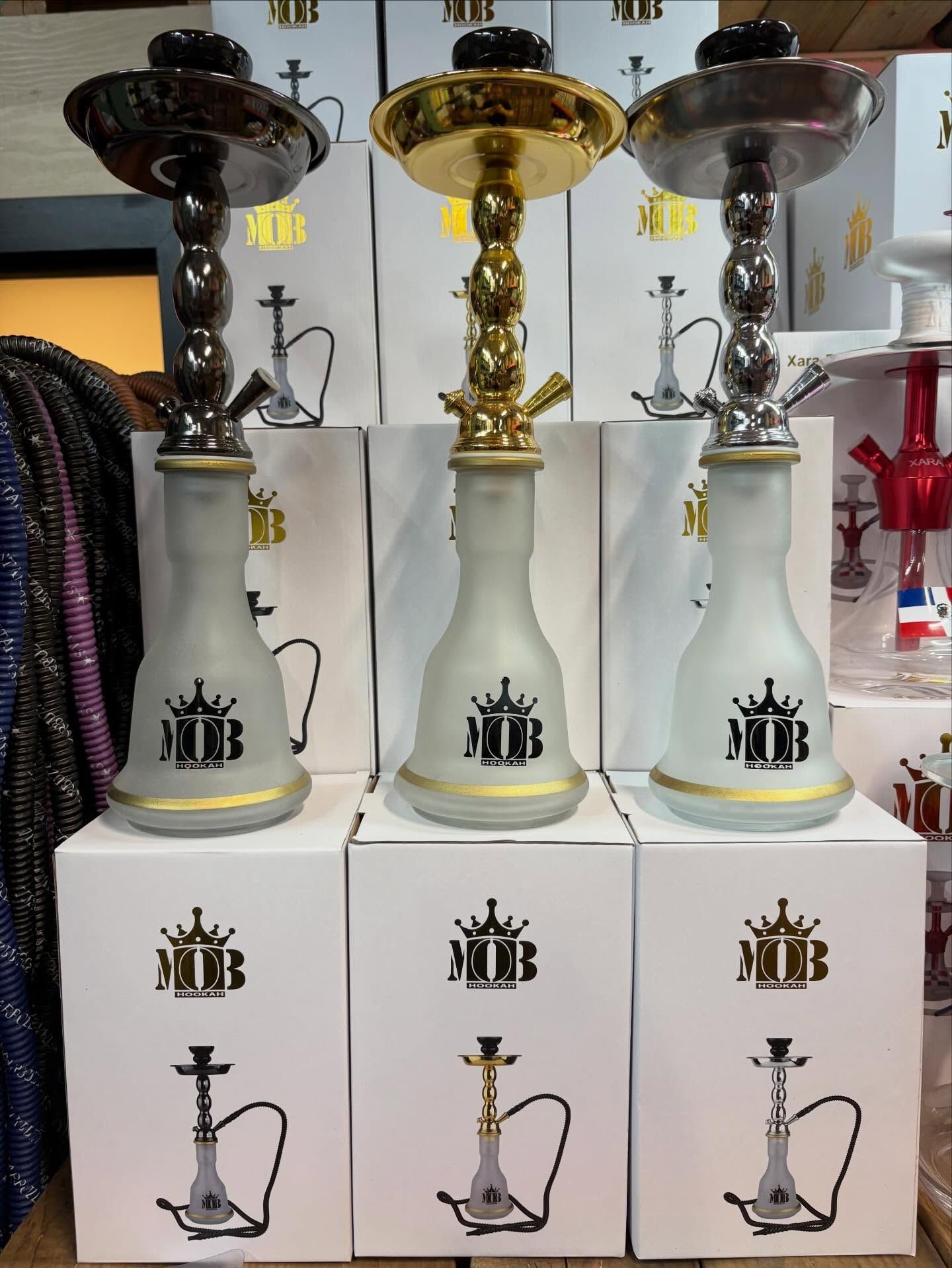 Three glass hookahs with metal stems and bases, on white boxes, displayed in a store.