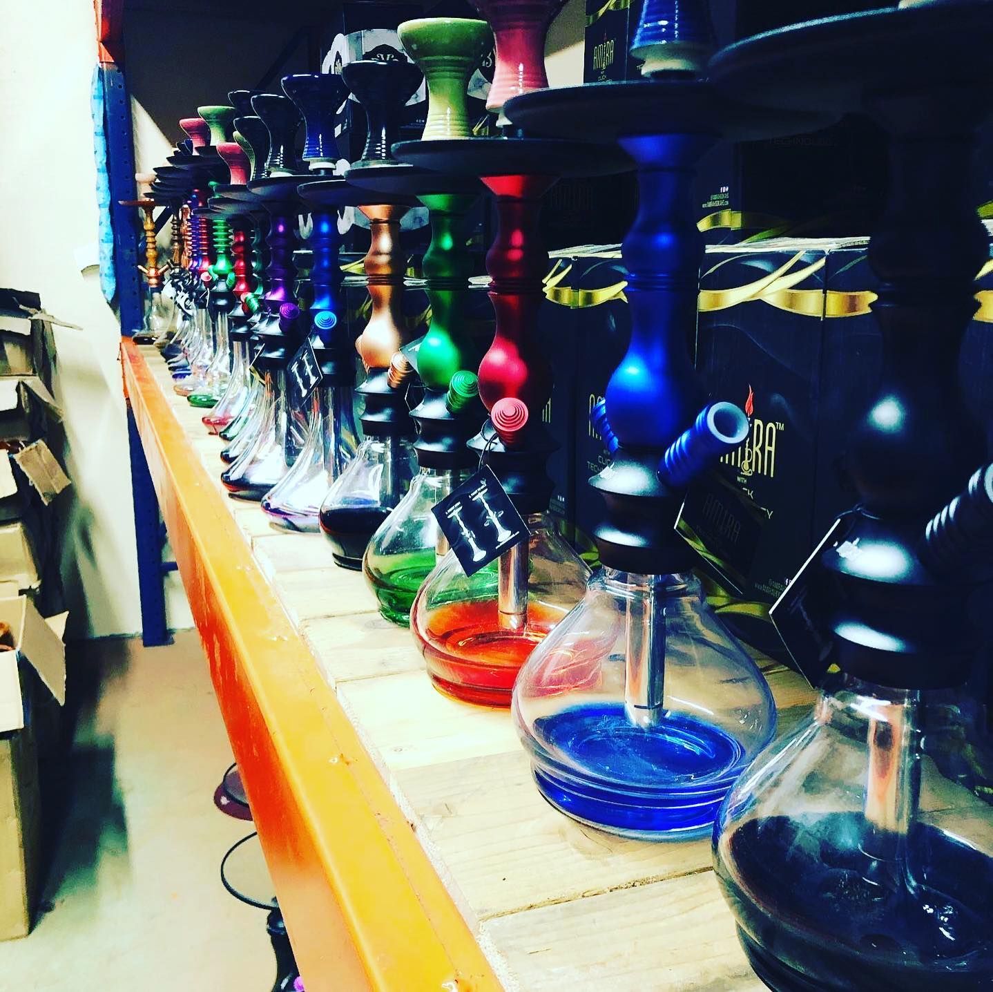 Row of colorful hookahs displayed on a wooden shelf in a store.