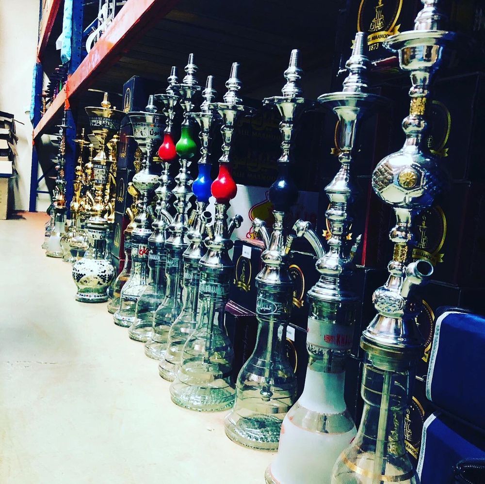 Row of hookahs with clear glass bases and silver metal stems, displayed on a shelf.