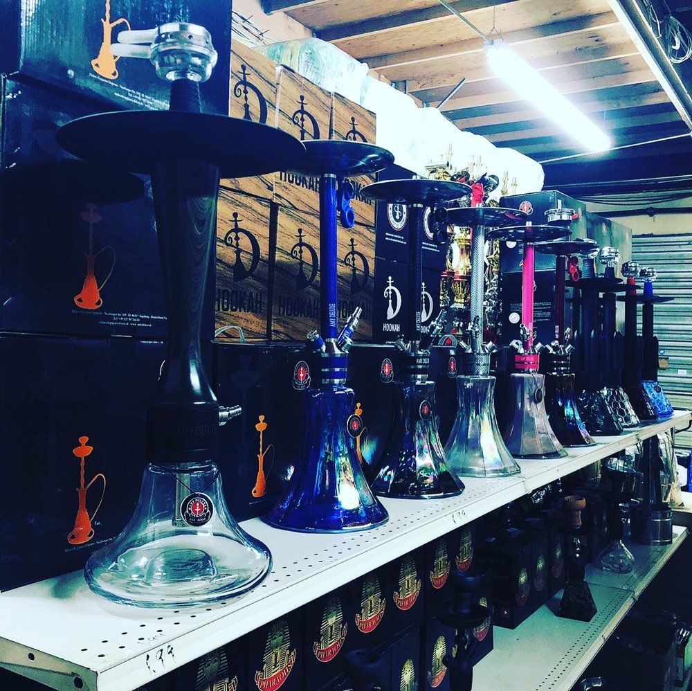 A row of colorful hookahs on a shelf, lit by a fluorescent light.