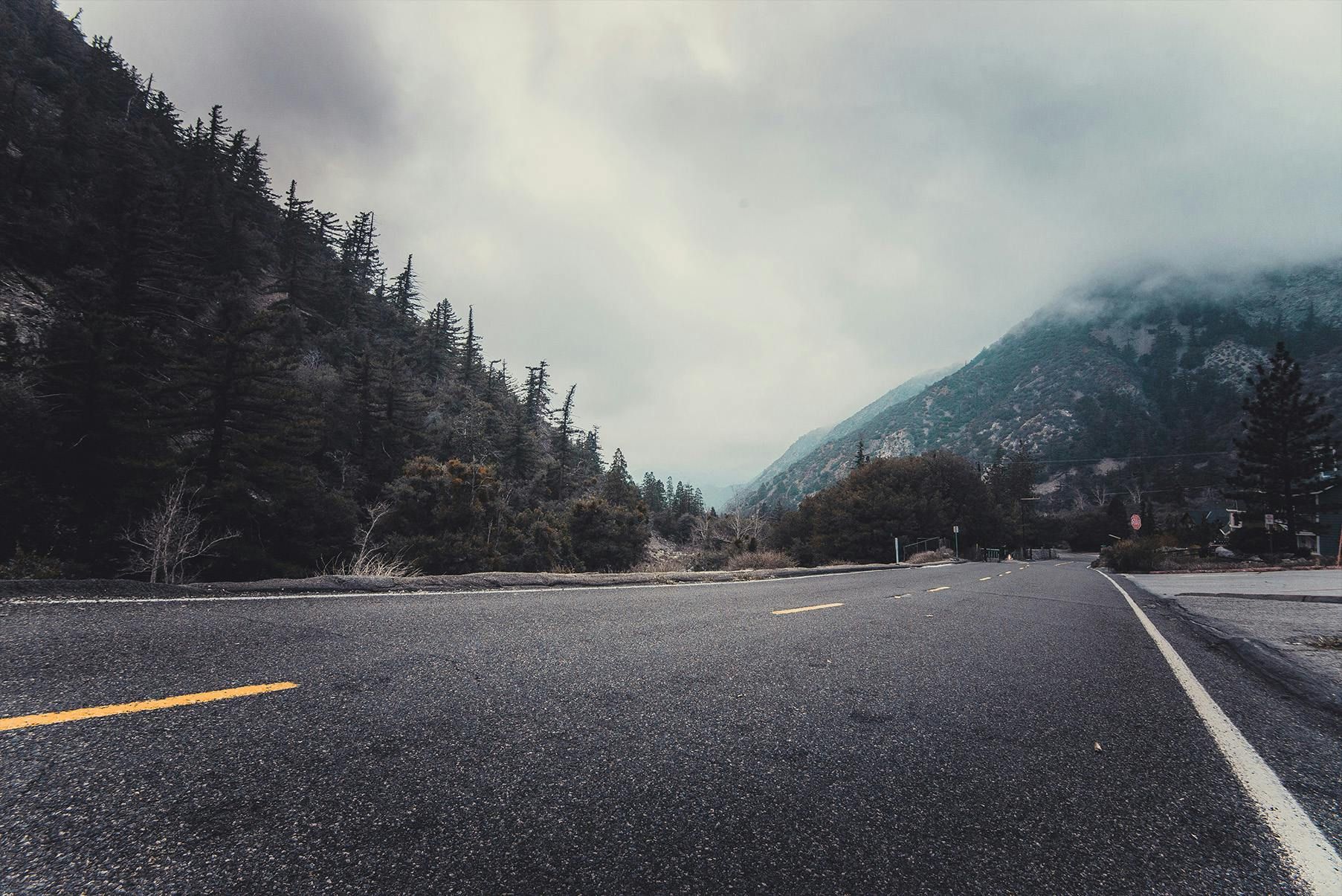 A road with mountains in the background and trees on the side.