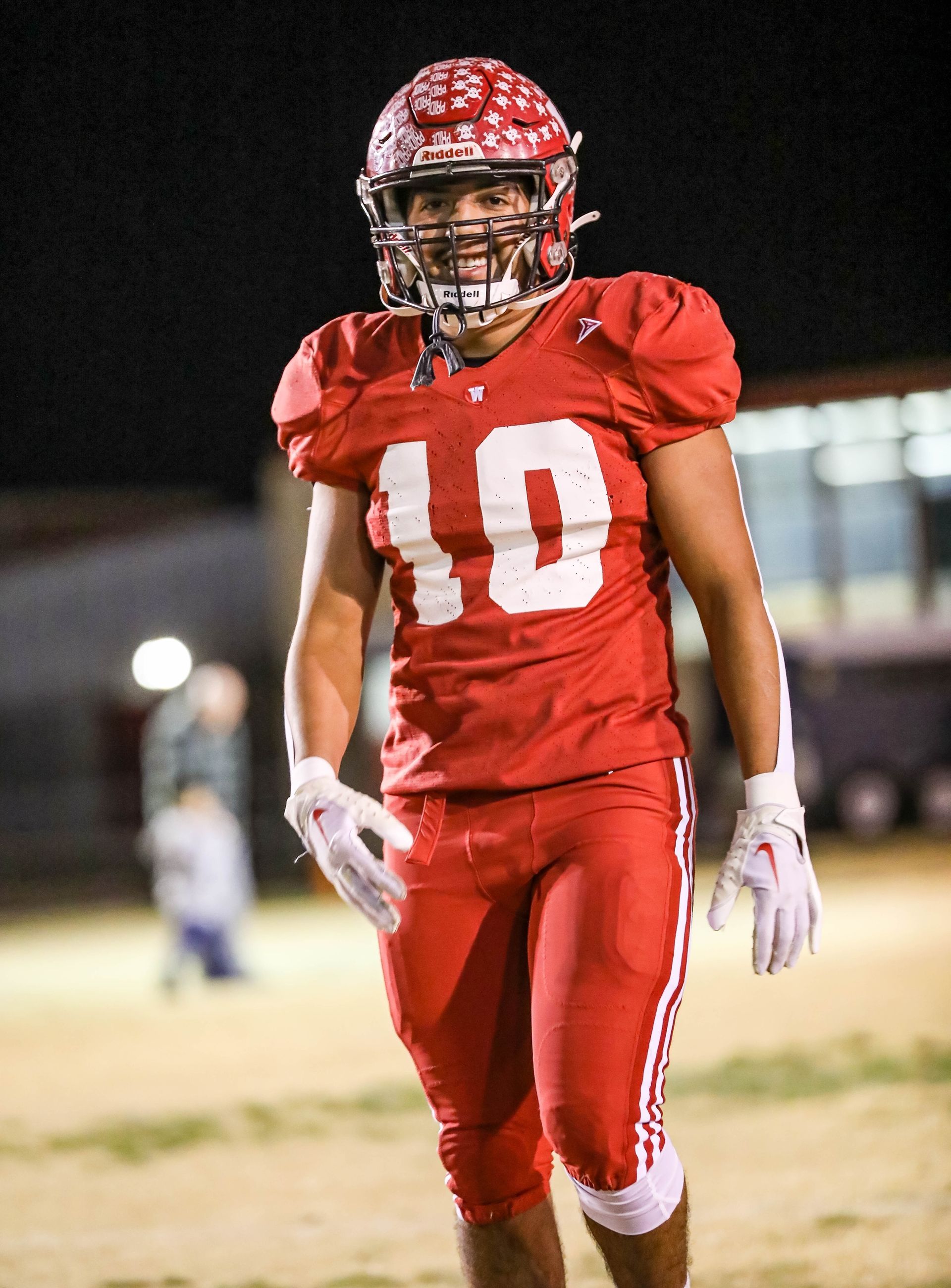 Football player in red uniform with number 10 smiling on a field at night.