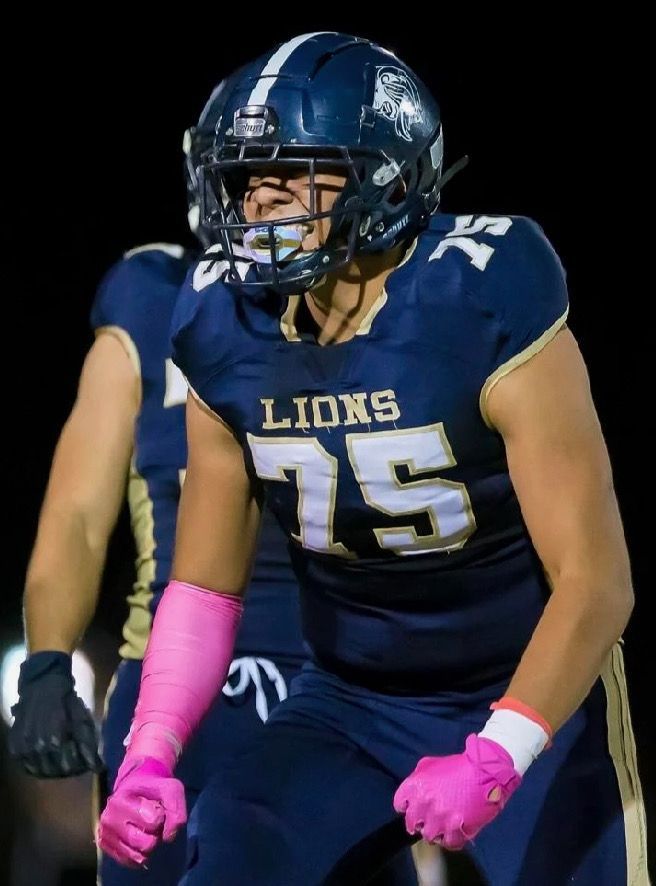Football player in a blue uniform with the number 75, wearing a helmet, pink wrist and hand wraps, with a focused expression.