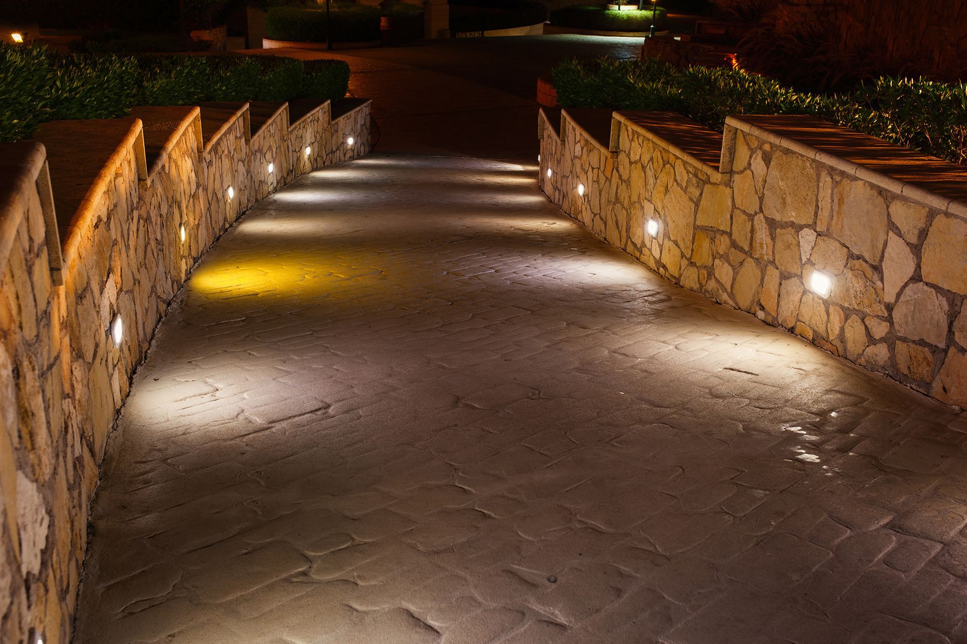 Stone pathway with inset lights between stone walls at night.