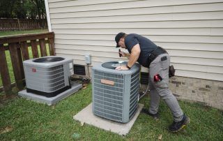 A man is working on an air conditioner outside of a house.