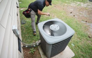 A man is working on an air conditioner outside of a house.