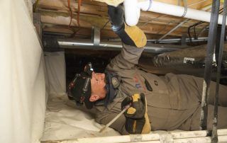 A man is crawling under a ceiling in a basement.