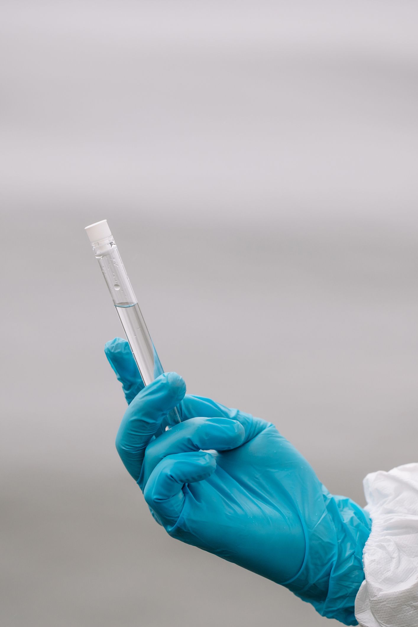 A person wearing blue gloves is holding a test tube.
