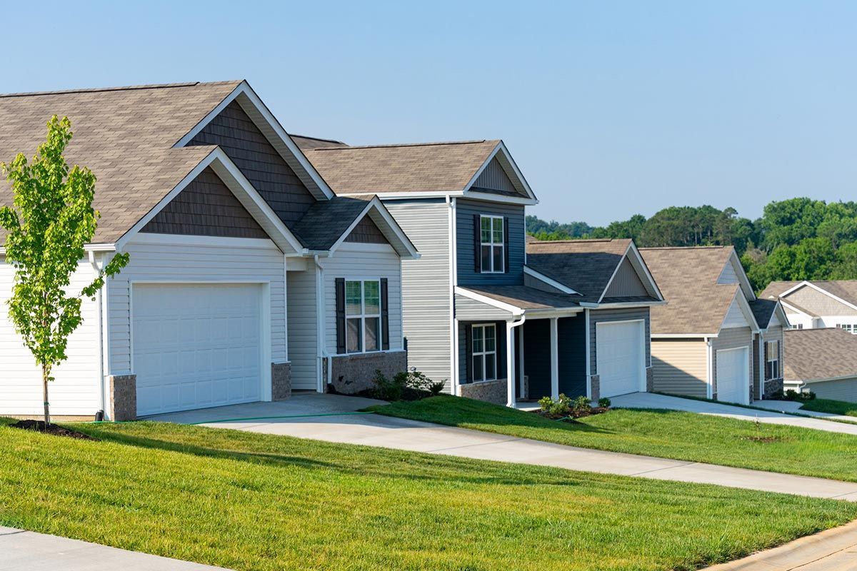 A white house with a brown roof is sitting on top of a lush green lawn.