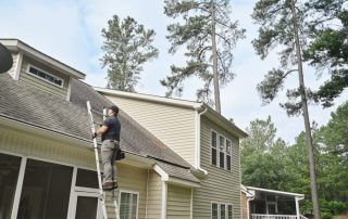 A man is standing on a ladder on the roof of a house.