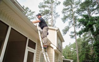 A man is standing on a ladder on the side of a house.