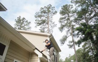 A man is standing on a ladder working on the roof of a house.