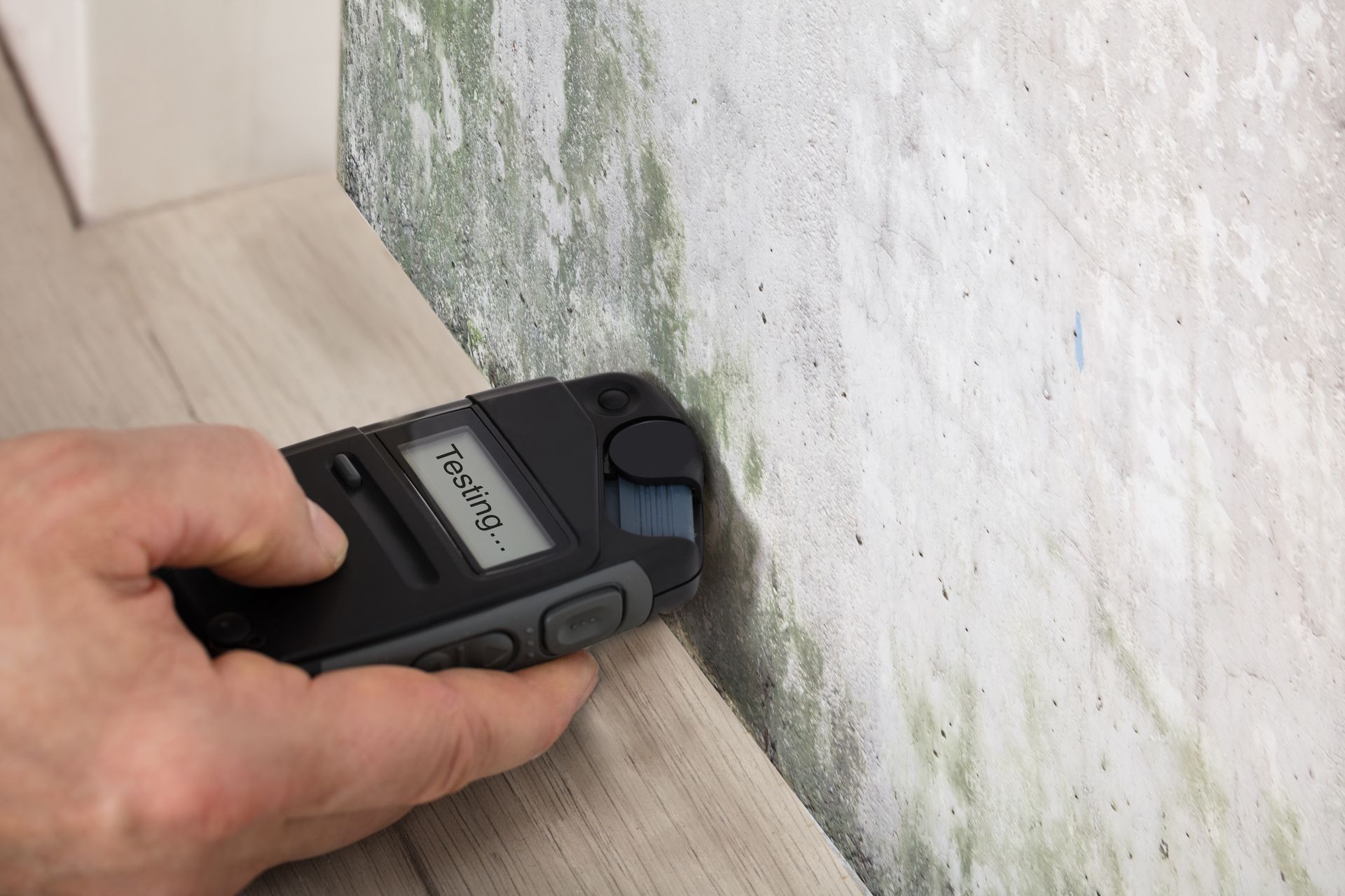 A person is using a moisture meter to check the humidity of a wall.