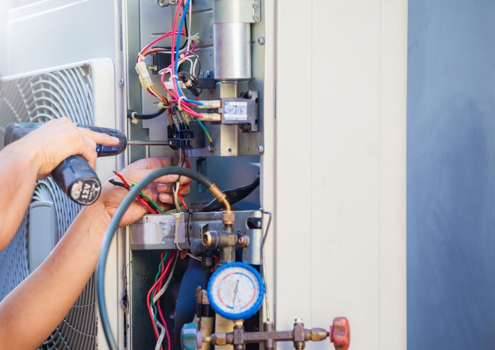 A Man is Working on an Air Conditioner With a Screwdriver — JW Electrical, Air & Solar Pty Ltd in Armidale, NSW