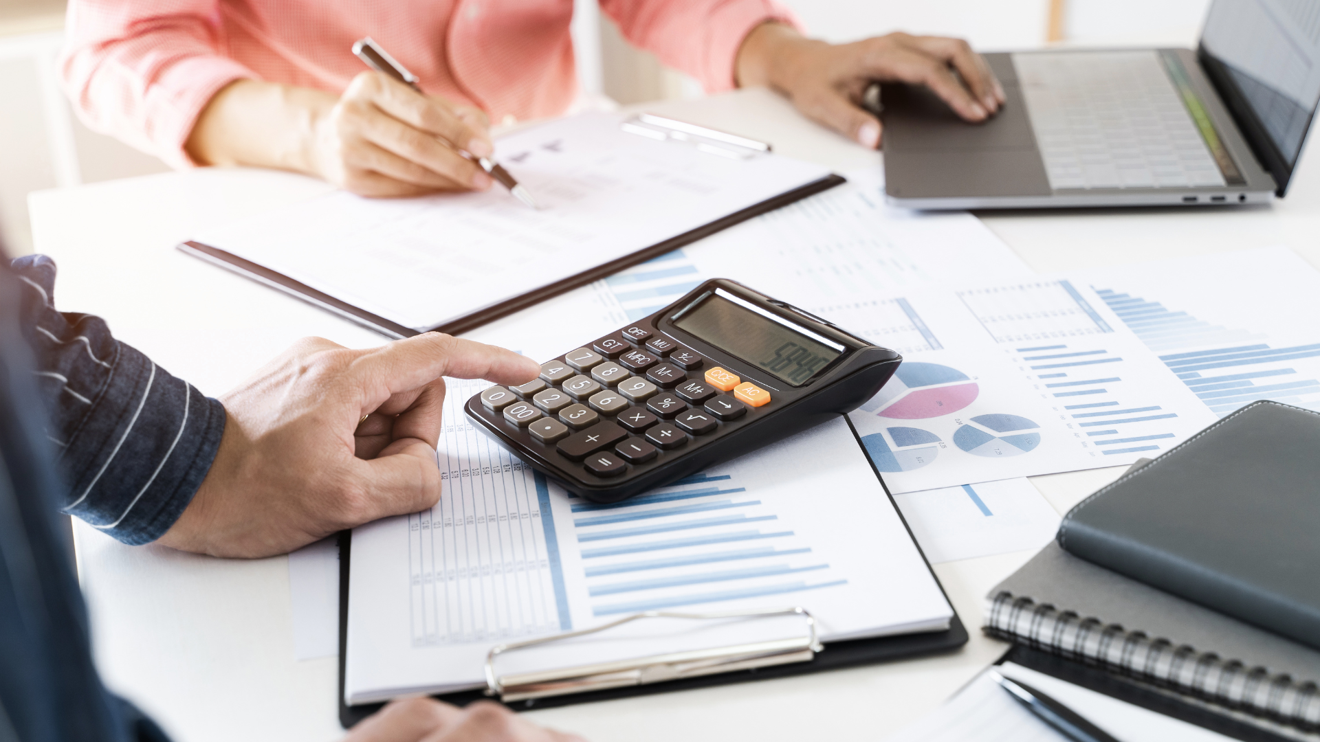 A man is pointing at a calculator while a woman is writing on a clipboard.