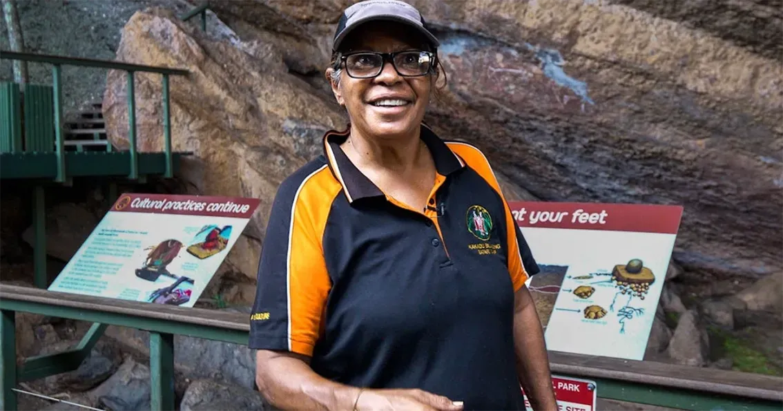 Smiling person in a black and orange shirt standing by exhibit signs in a rocky outdoor setting — Kakadu Billabong Safari Camp in Kakadu, NT
