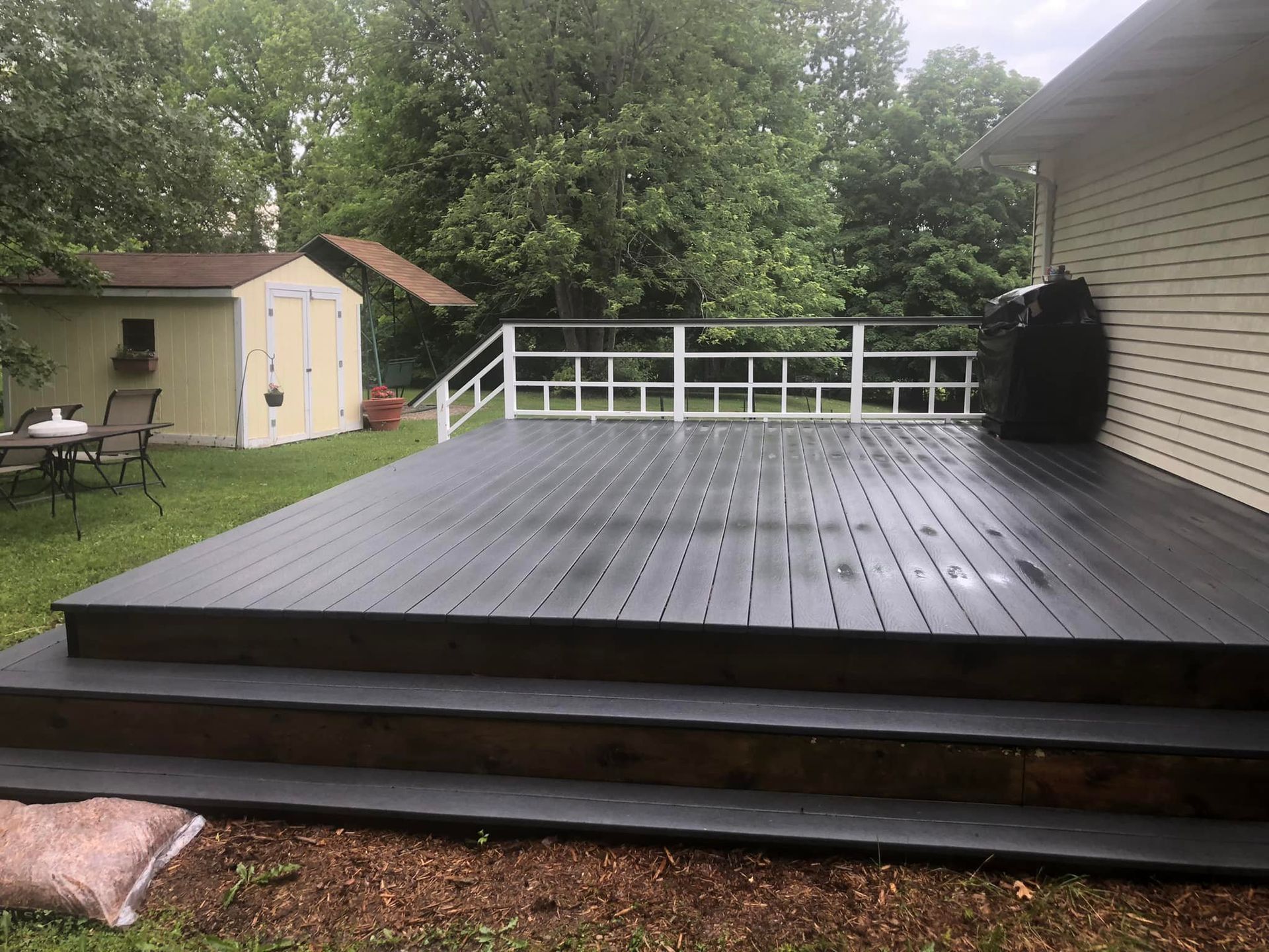 A black deck with stairs leading up to it is in the backyard of a house.