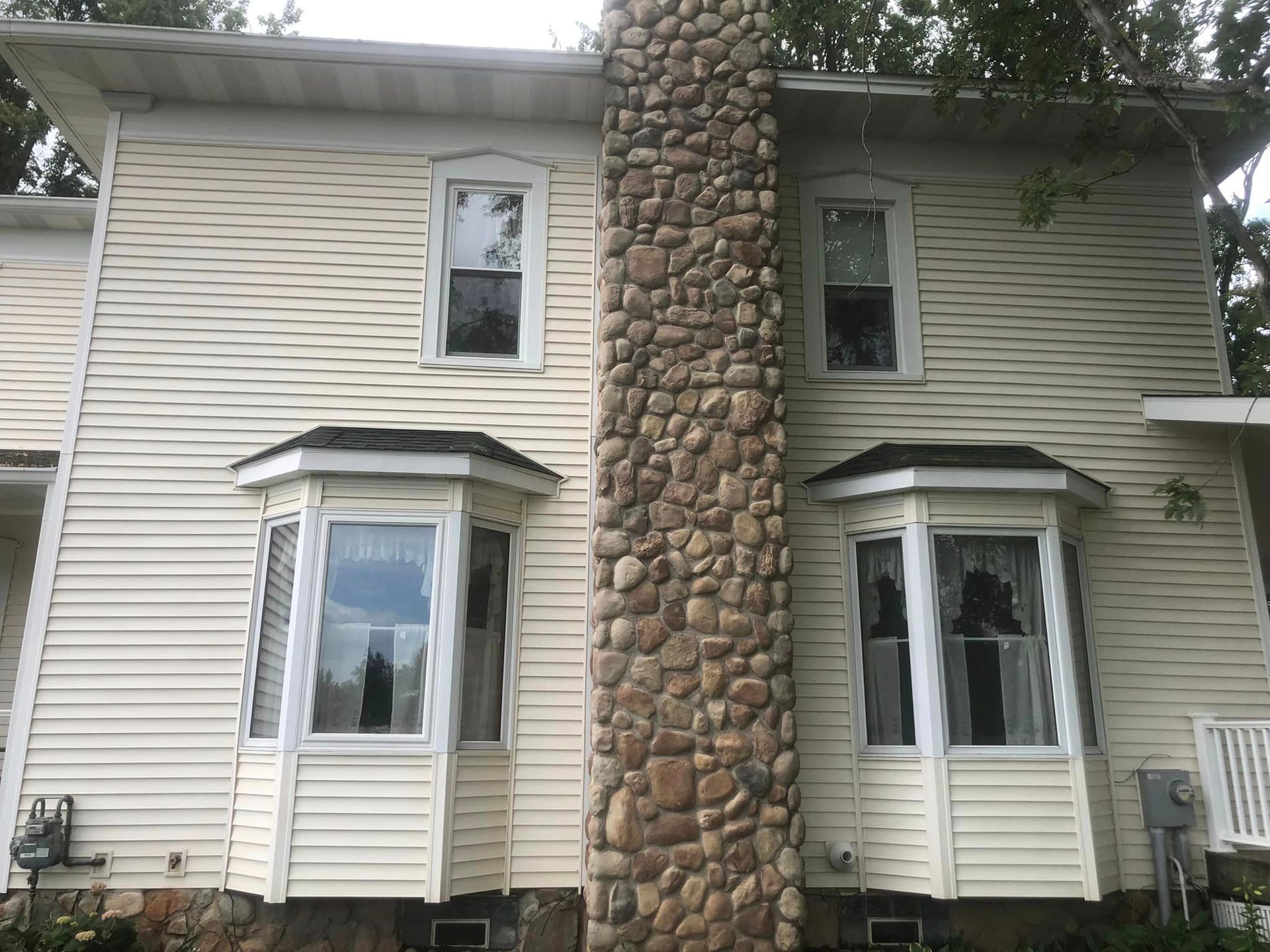 A white house with a stone chimney and bay windows.