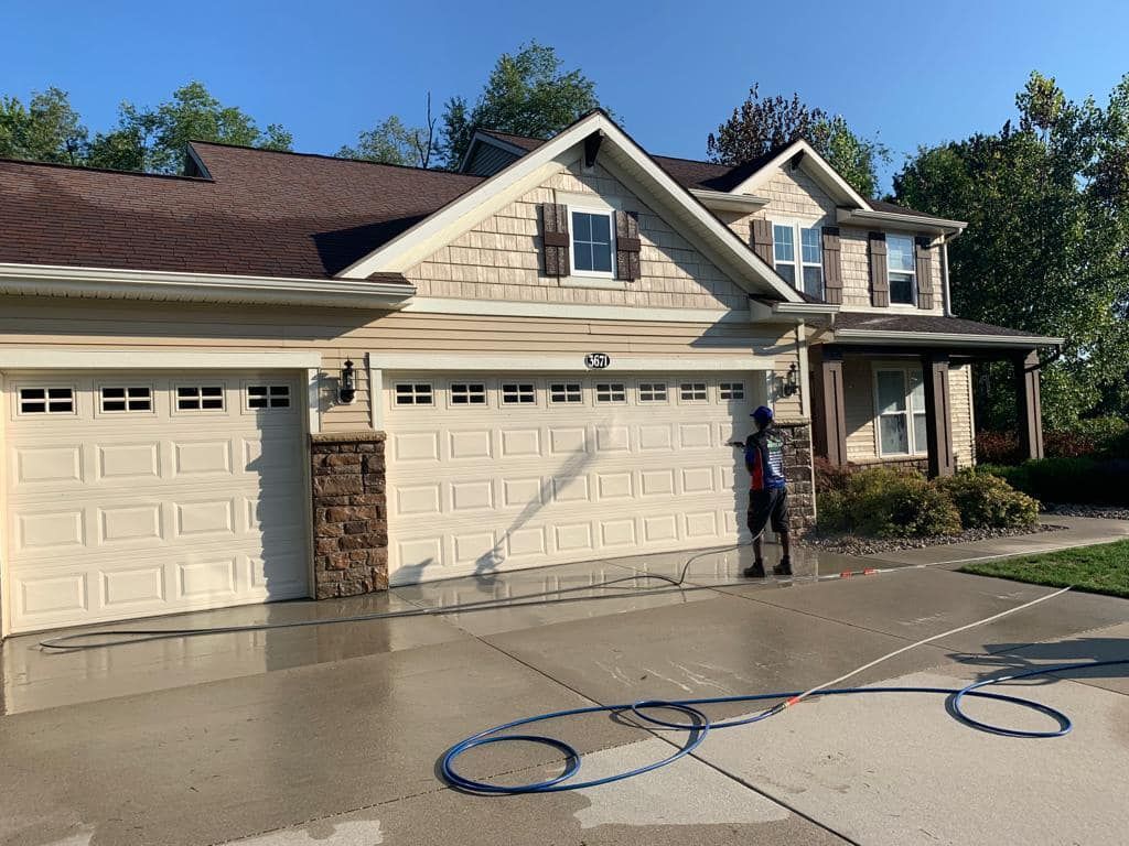 A man is washing the driveway of a large house.