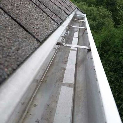 A close-up of a gutter on a roof with trees in the background.