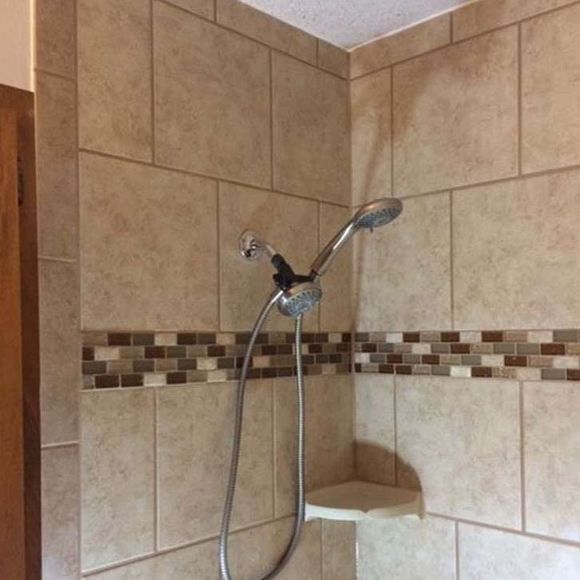 Tiled shower with a hand-held showerhead and corner shelf. Beige and brown tiles.